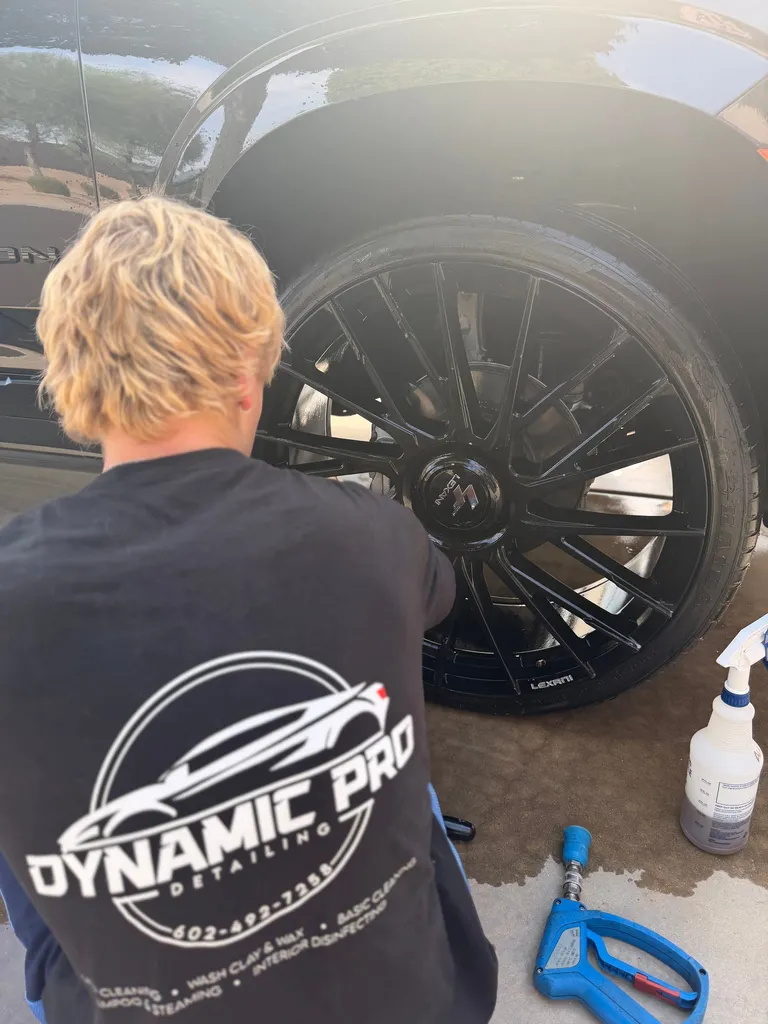 Detailer cleaning a gloss-black wheel on a freshly washed black SUV