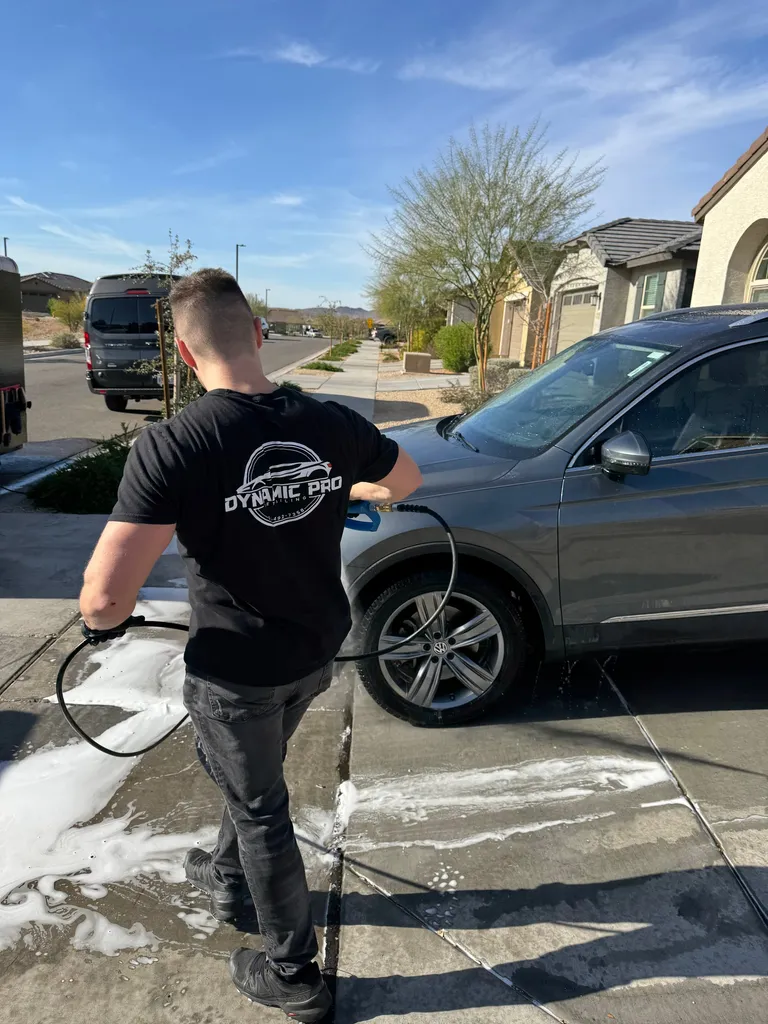 Detailer pressure-rinsing a Volkswagen SUV in a customer's driveway