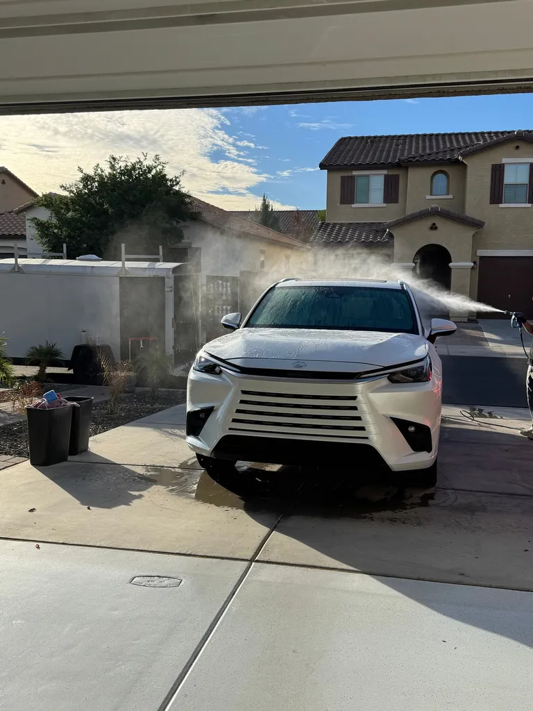 Pressure-rinsing a white Lexus SUV in a customer's driveway