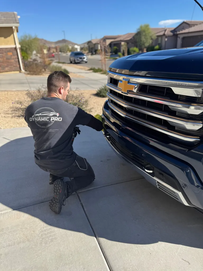 Detailer wiping down the chrome grille of a Chevrolet Silverado in a customer's driveway