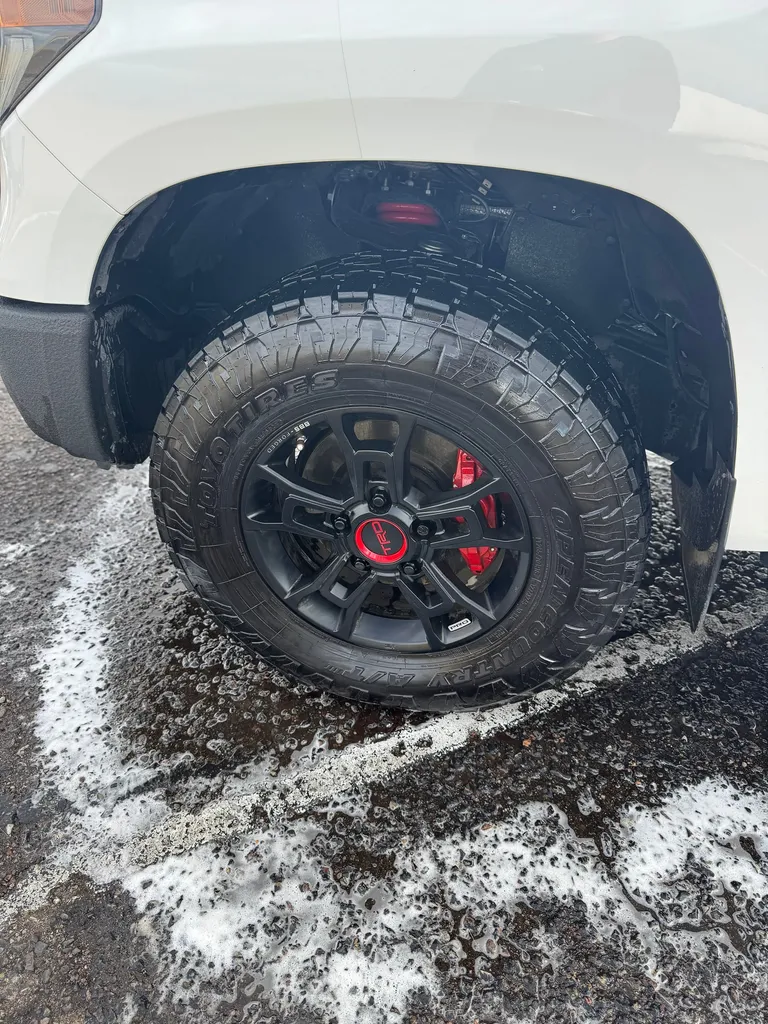 Black truck wheel with red brake calipers during a foam wash